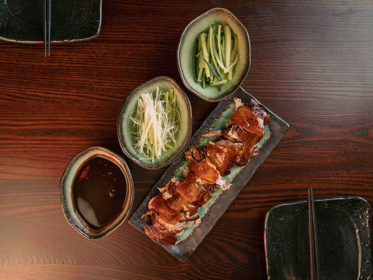 Sliced Peking duck with bowls of hoisin, cucumber and spring onion.
