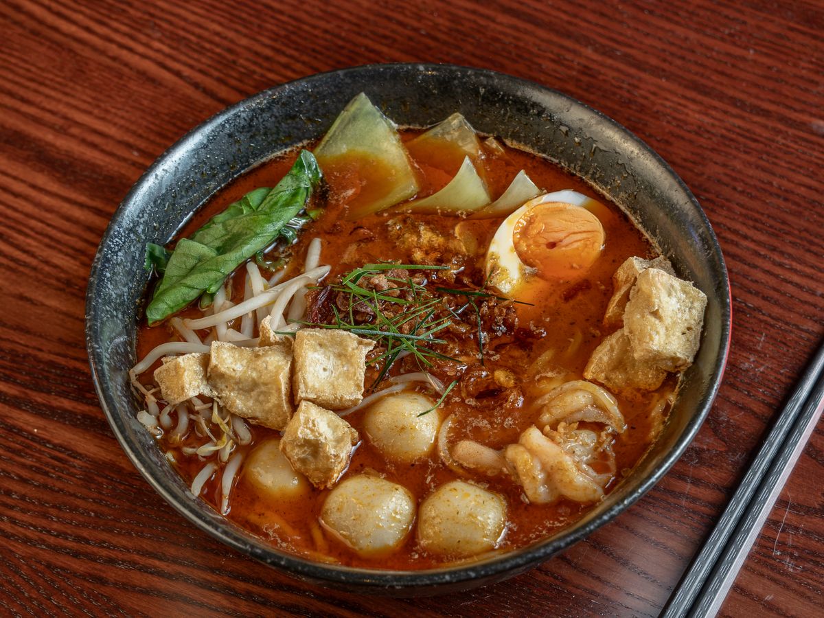 A bowl of seafood laksa with tofu, fish balls, a soft egg and bean sprouts.