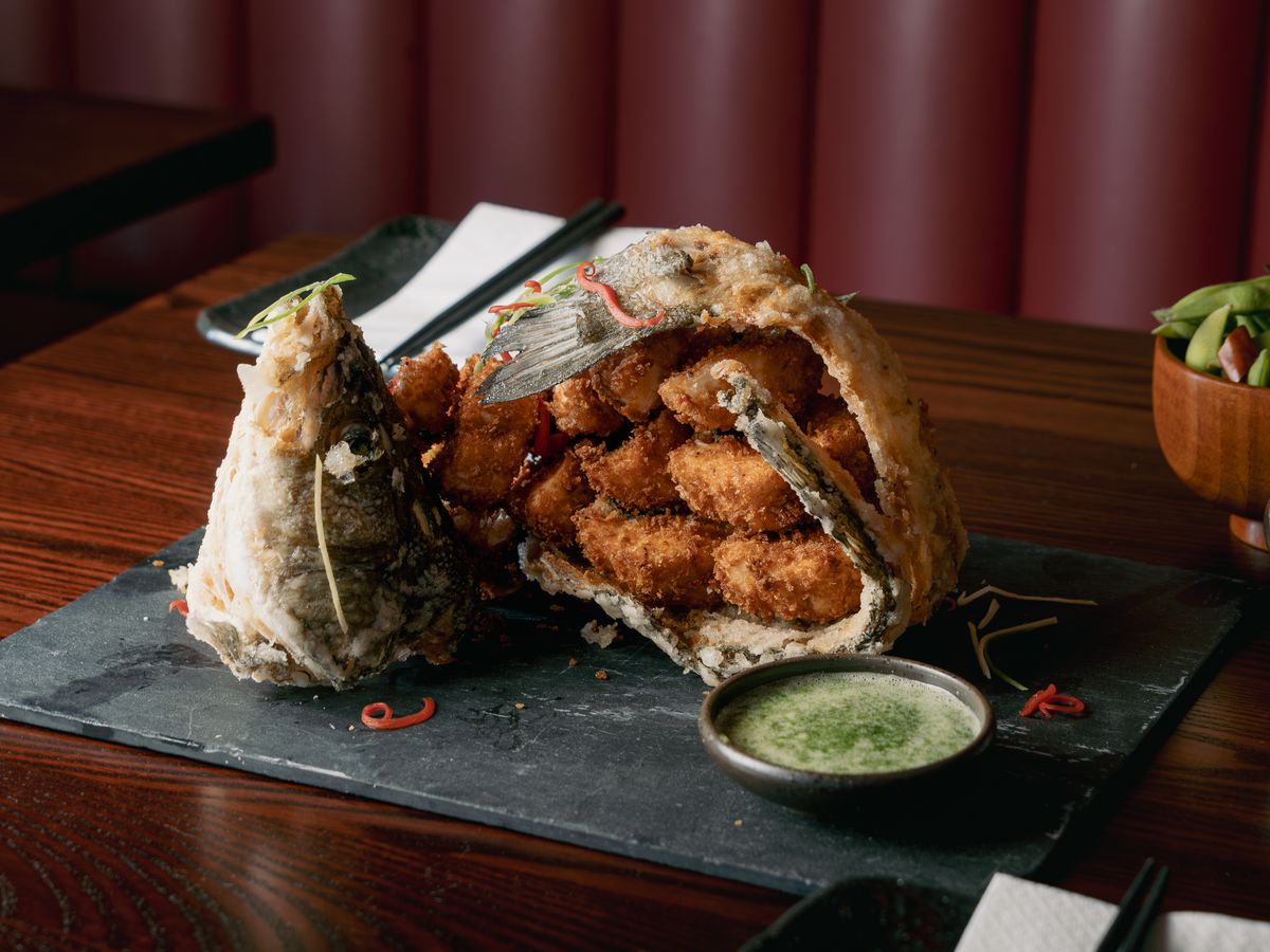 A whole sea bass fried in panko and opened up on a slate, with a wasabi avocado dip.