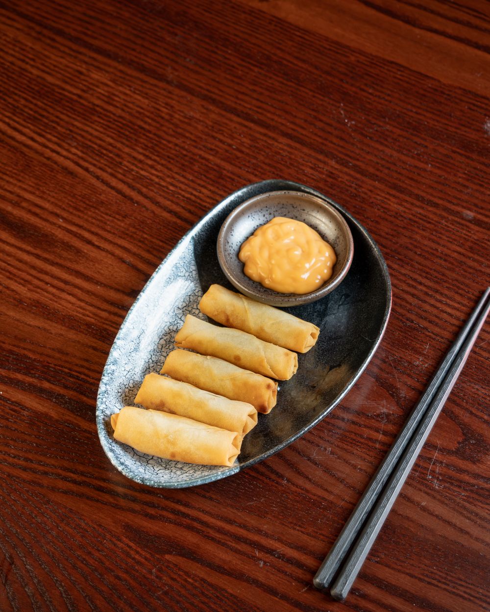 Four golden vegetable spring rolls with a dipping sauce.
