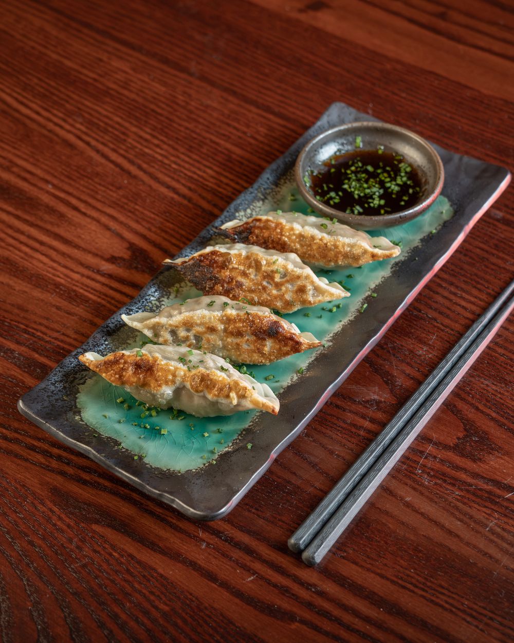 Five pan-fried gyoza on a teal plate with a dipping sauce.