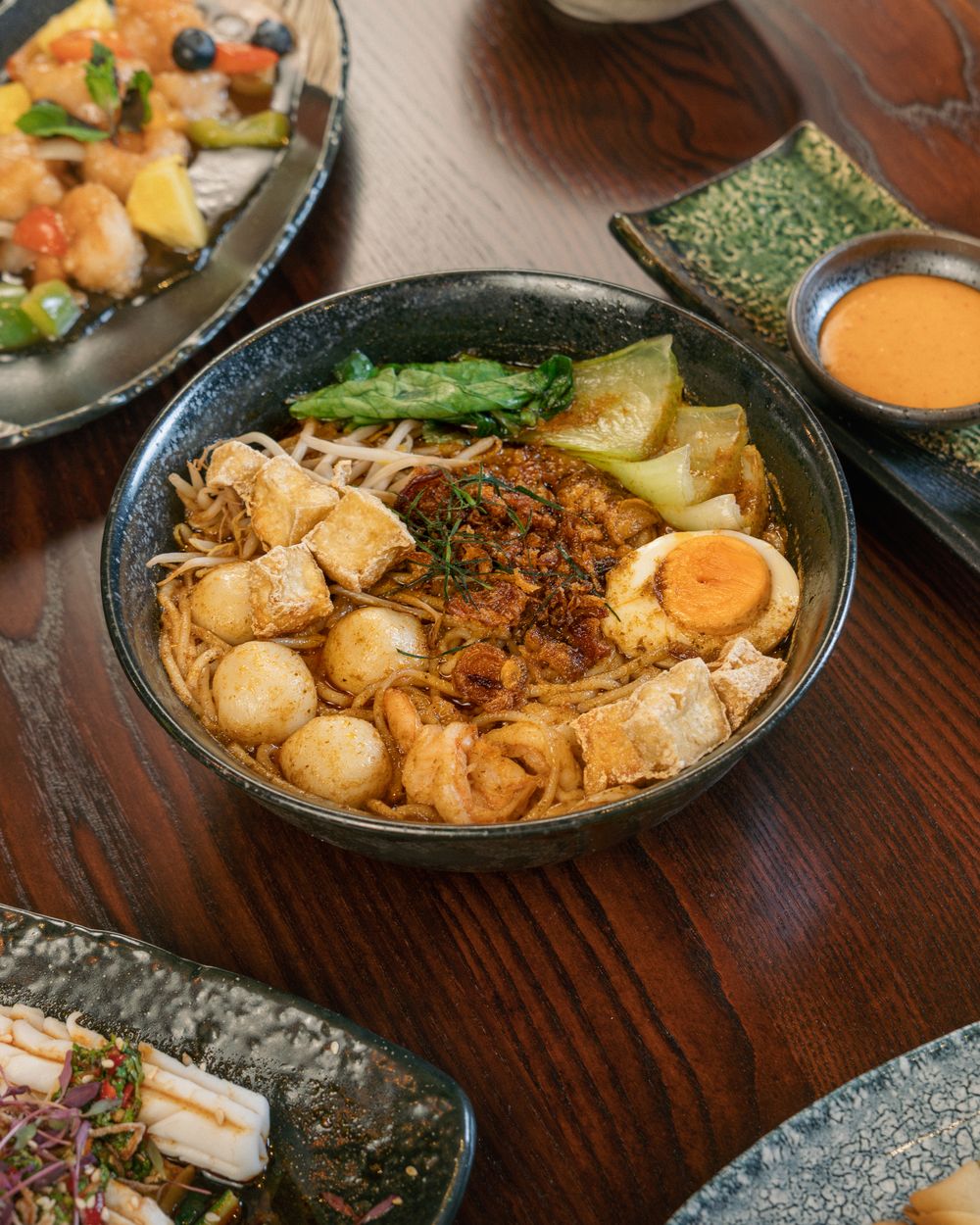 A bowl of seafood laksa with tofu, fish balls, a soft egg and bean sprouts.