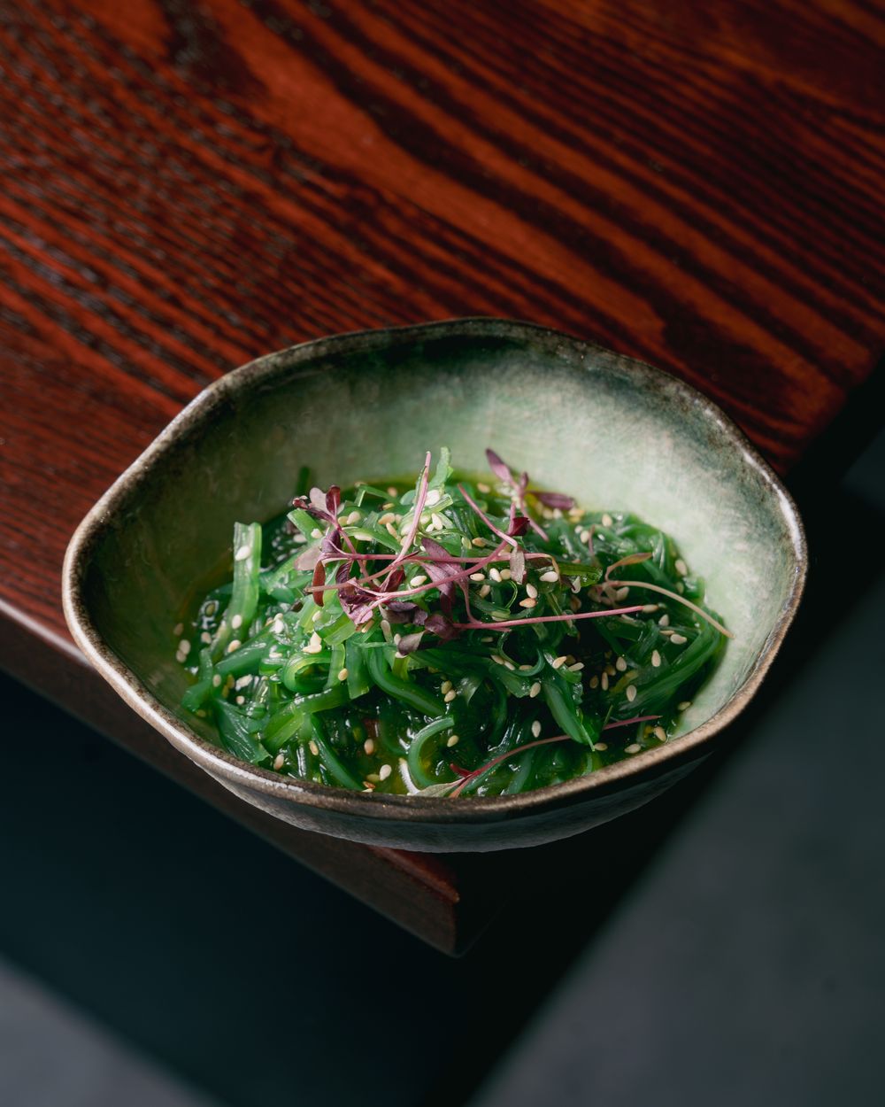Wakame salad with sesame and micro herbs in a green glazed bowl.