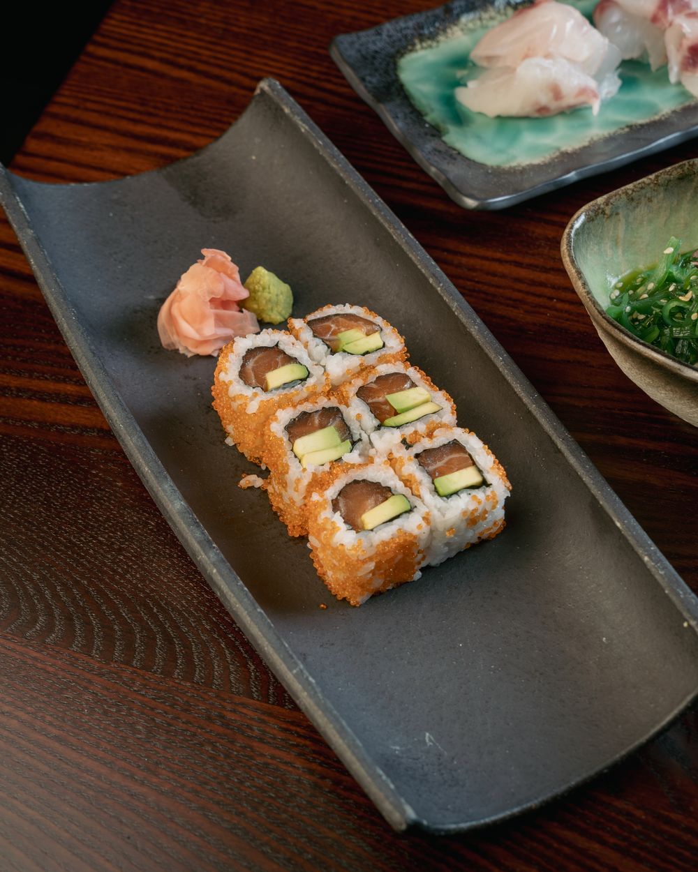 A sushi roll of salmon and avocado with pickled ginger and wasabi.